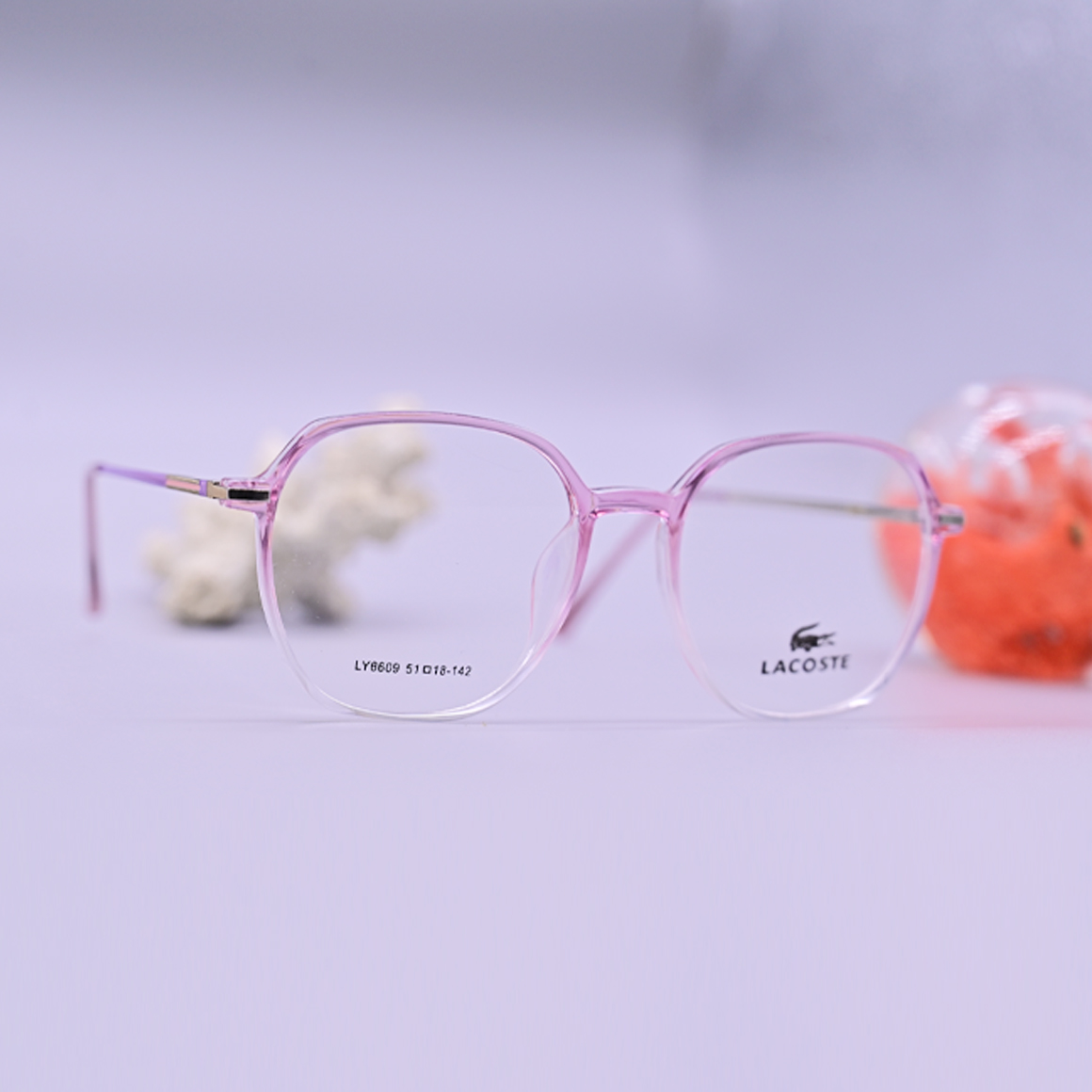 نظارة طبية من ماركة لاجوست موديل 6609، إطار دائري كامل بلون وردي شفاف وأذرع معدنية نحيفة، متوفرة لدى متجر عين العون في اليمن.